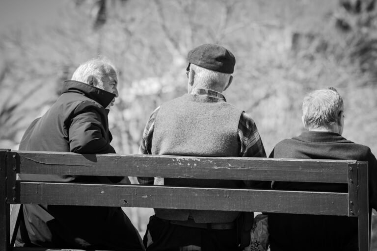 Three senior men enjoying a conversation on a park bench. Black and white imagery.